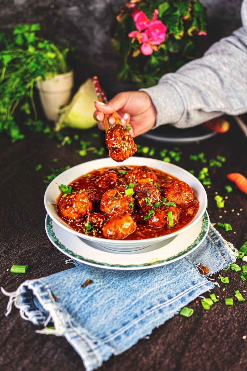 Close up of veg manchurian ball held with chopsticks, showing glossy garlic sauce coating and crispy texture