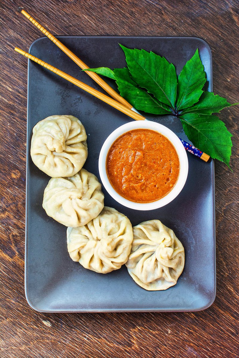 a plate of veg momos and a bowl of spicy momos chutney on a table