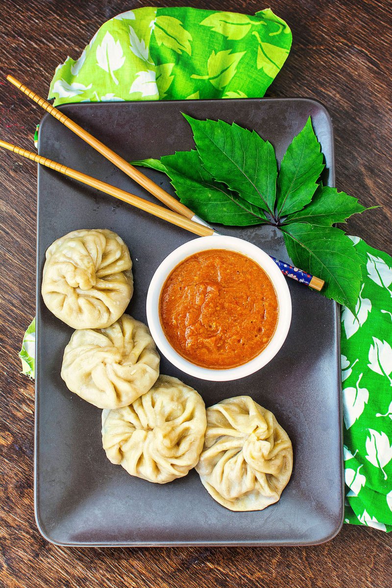 a brown plate of veg momos and a bowl of spicy momos chutney on a table
