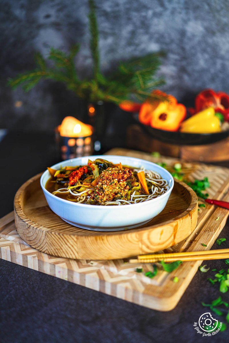 a bowl of veg thukpa soup noodles with vegetables and chopsticks on a cutting board and candle in background