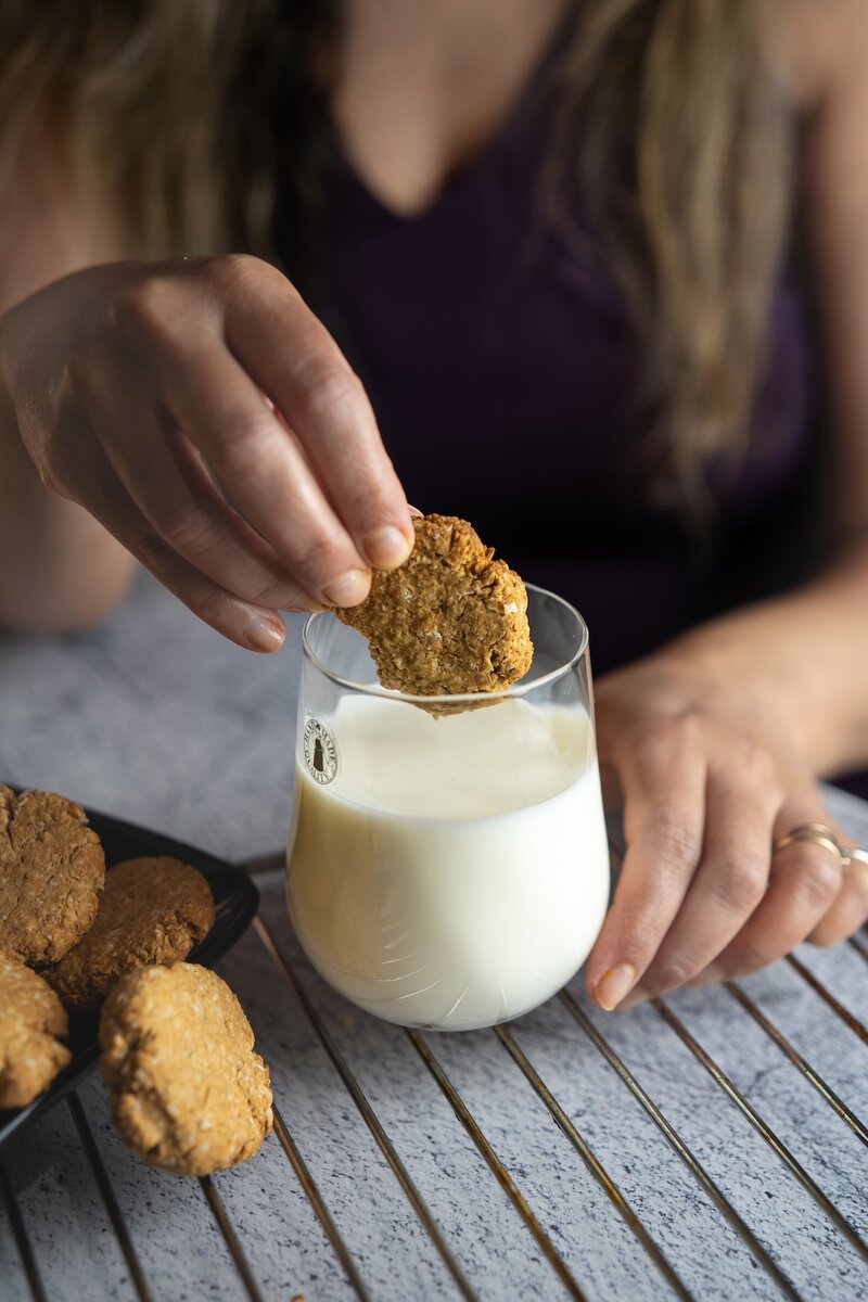 Vegan oatmeal cookie being dipped into a glass of oat milk, healthy dairy free cookies made with oats and peanut butter.