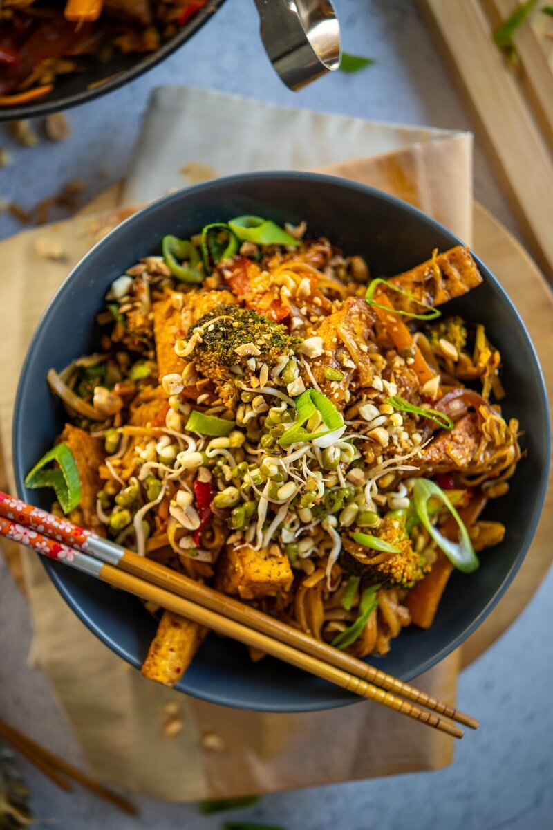 Vegan Pad Thai noodles with crispy tofu, broccoli, and bean sprouts served in a bowl with chopsticks, gluten free and plant based.