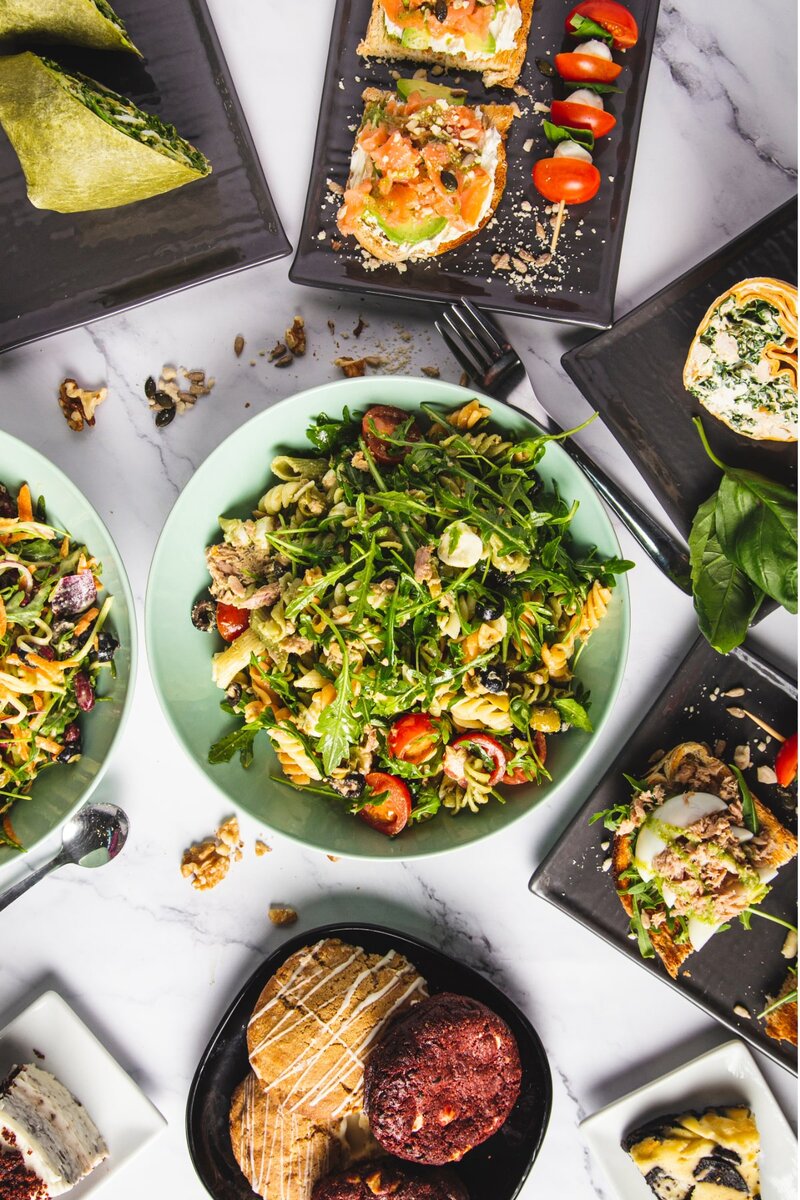 Healthy gourmet salad platter with fresh greens, cherry tomatoes, artisan bread, pastries, and assorted appetizers on a marble table — delicious vegetarian lunch spread
