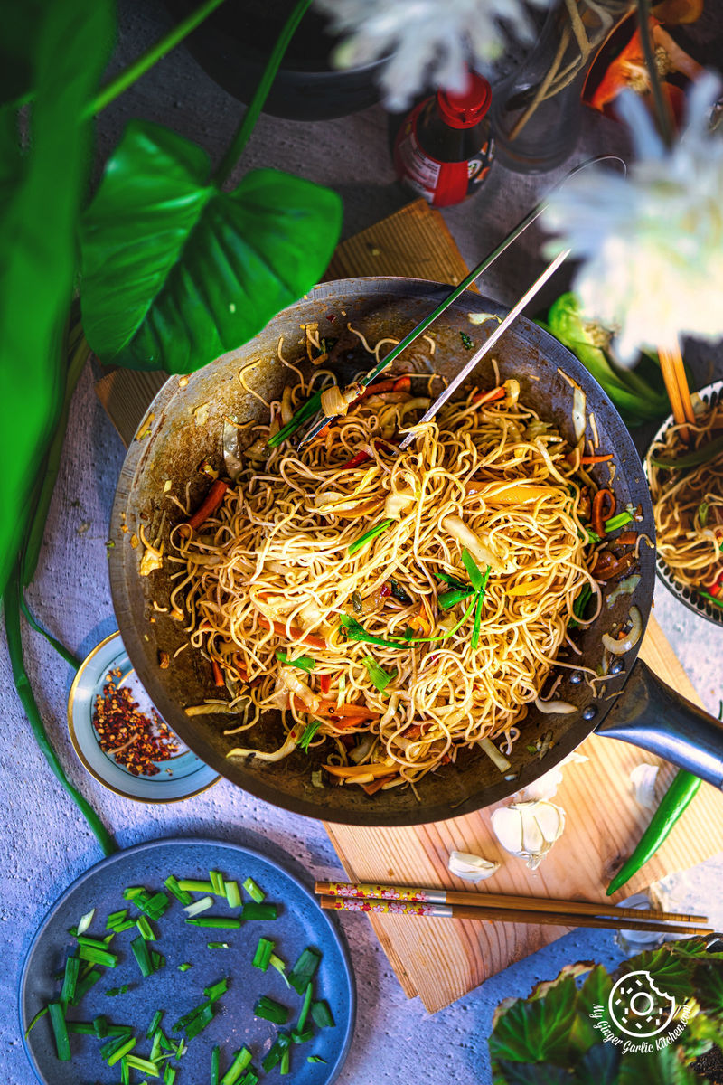 overhead shot of a wok with hakka noodles with green onions on the side