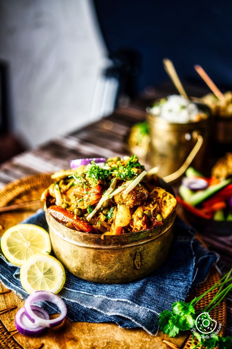 vegetable jalfrezi served in a brass bowl with lemon slices on the side