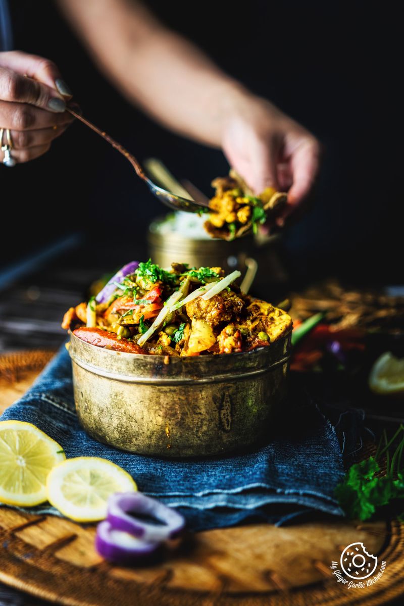 a hand taking vegetable jalfrezi from brass bowl