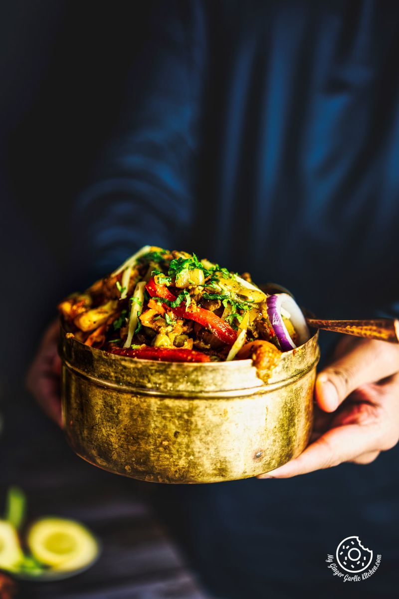 a person holding vegetable jalfrezi served in a brass bowl