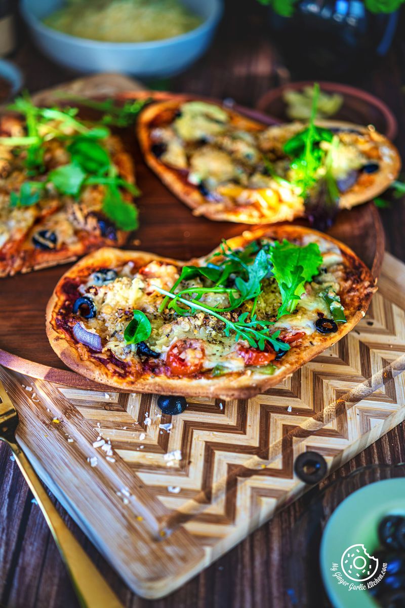 3 vegetarian heart pizza decorated with green leaves sitting on top of a wooden table