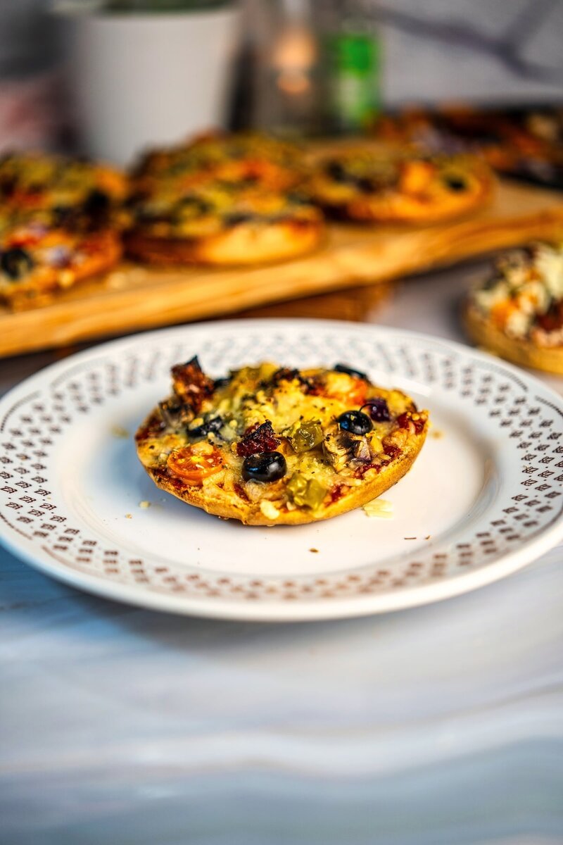 Single serving homemade bun pizza with olives and cheese on a white decorative plate, quick vegetarian meal idea