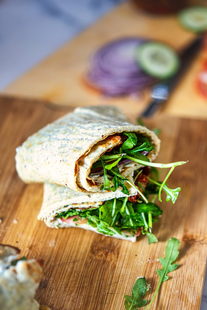 A delicious wrap made from viral cottage cheese flatbread, filled with fresh arugula, sliced onions, tomatoes, cucumbers, and sun-dried tomatoes.