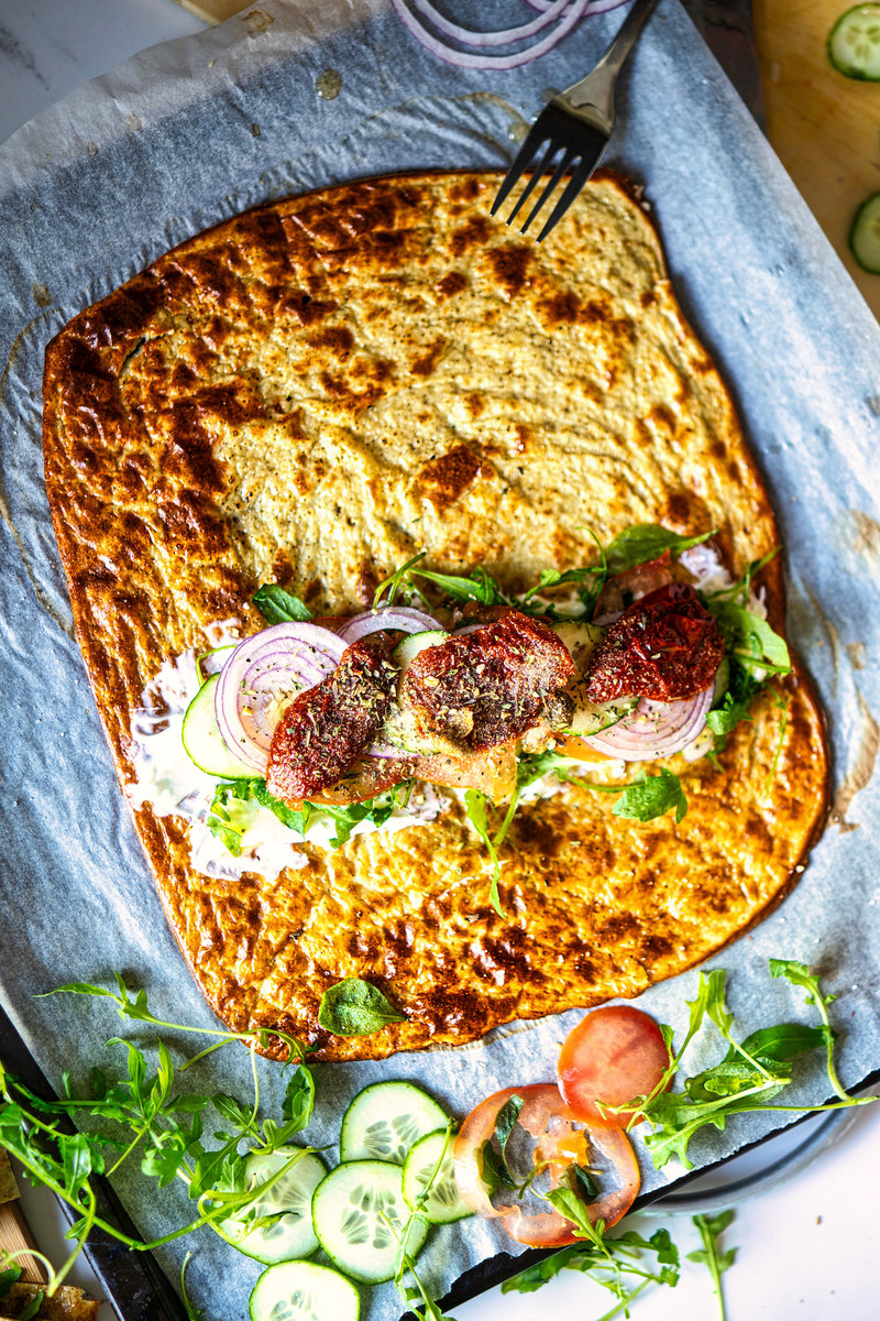 Viral cottage cheese flatbread topped with a creamy layer of cream cheese, fresh arugula, red onion slices, juicy tomato slices, crisp cucumber slices, and flavorful sun-dried tomatoes.