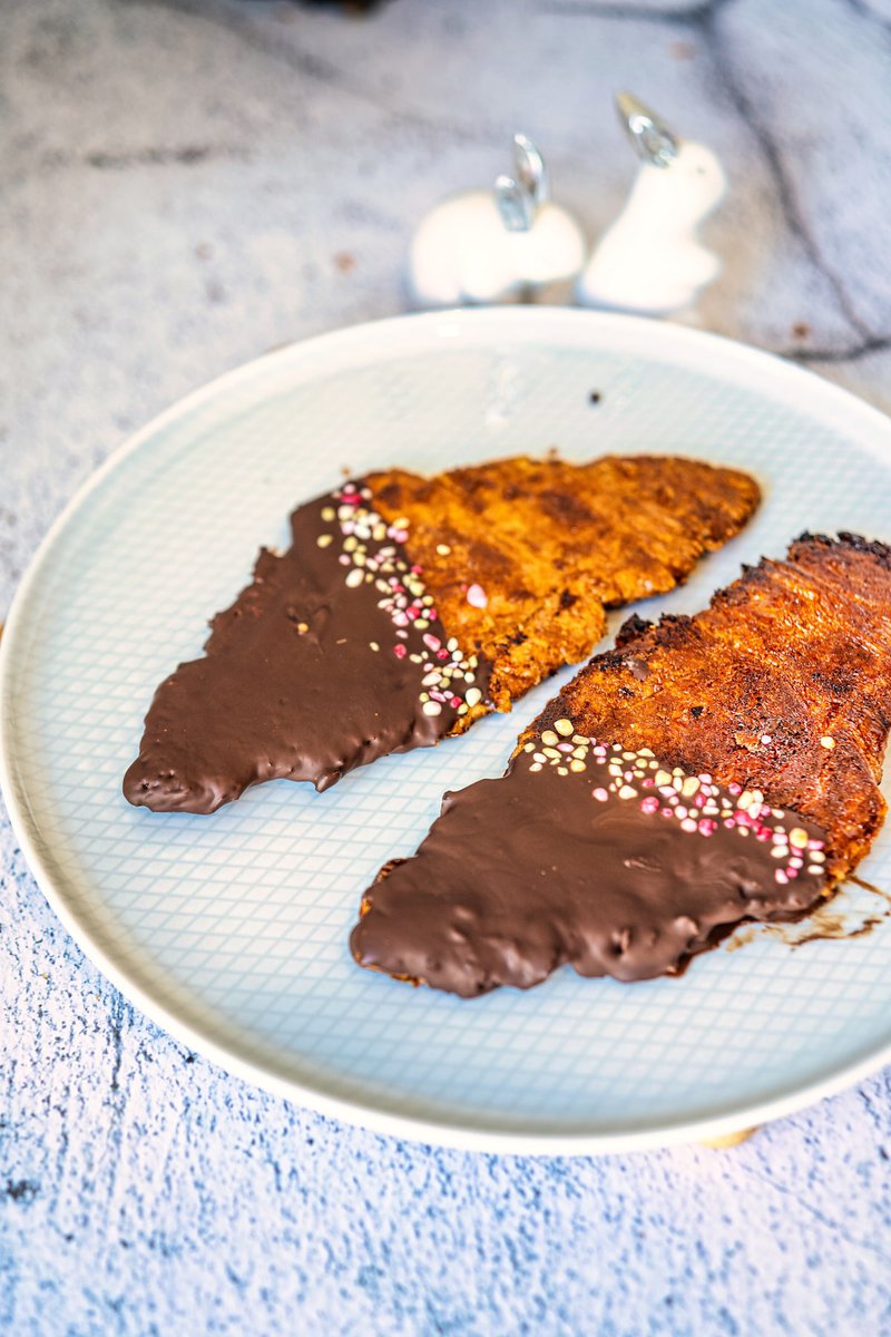Close-up of two flat, chocolate-covered croissants with sprinkles, placed on a ceramic plate with a patterned design.