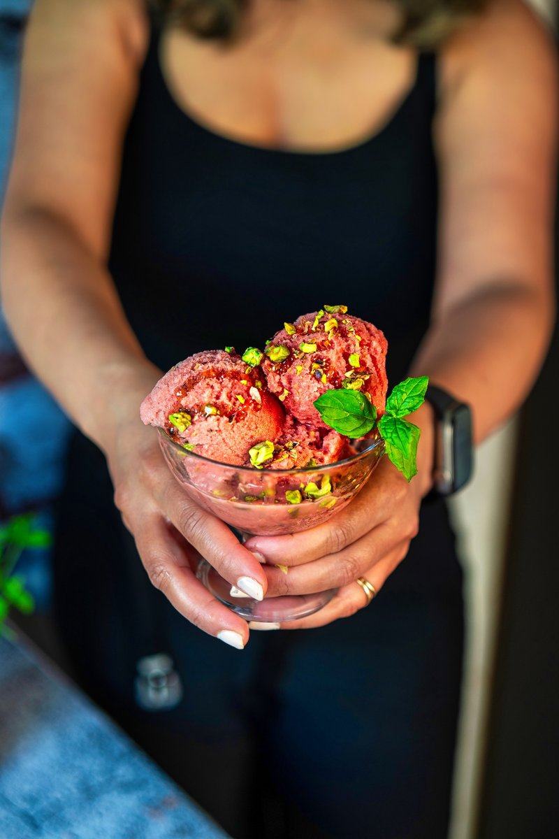 Person holding a frozen mini watermelon filled with Viral Watermelon Ice Cream, garnished with fresh mint and pistachios