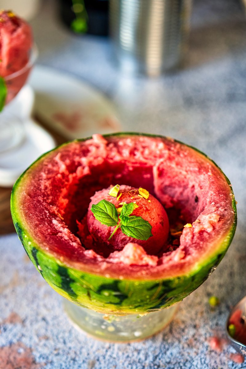 Person holding a bowl of Viral Watermelon Ice Cream topped with chopped pistachios, maple syrup drizzle, and fresh mint