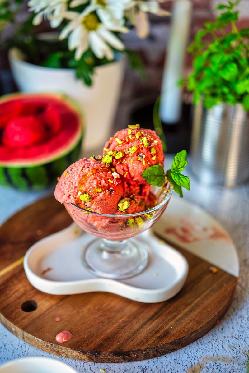 Viral Watermelon Ice Cream served in a glass dessert bowl with chopped pistachios, maple syrup drizzle, fresh mint, and frozen watermelon in the background