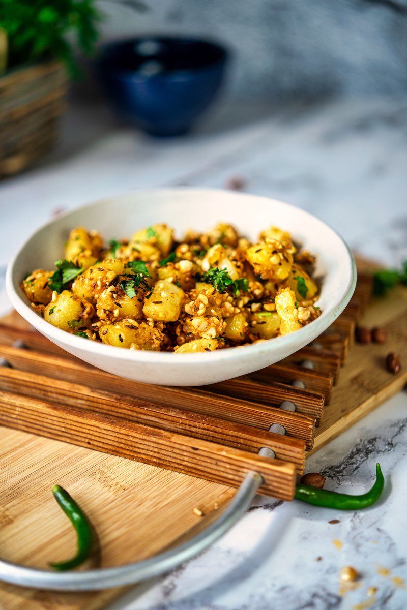 A bowl of vrat wale aloo, garnished with fresh coriander, served on a wooden board with green chilies.