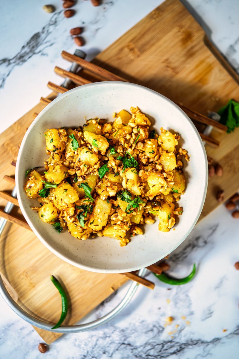 A overhead view of a bowl of vrat wale aloo garnished with cilantro and peanuts, placed on a wooden board.