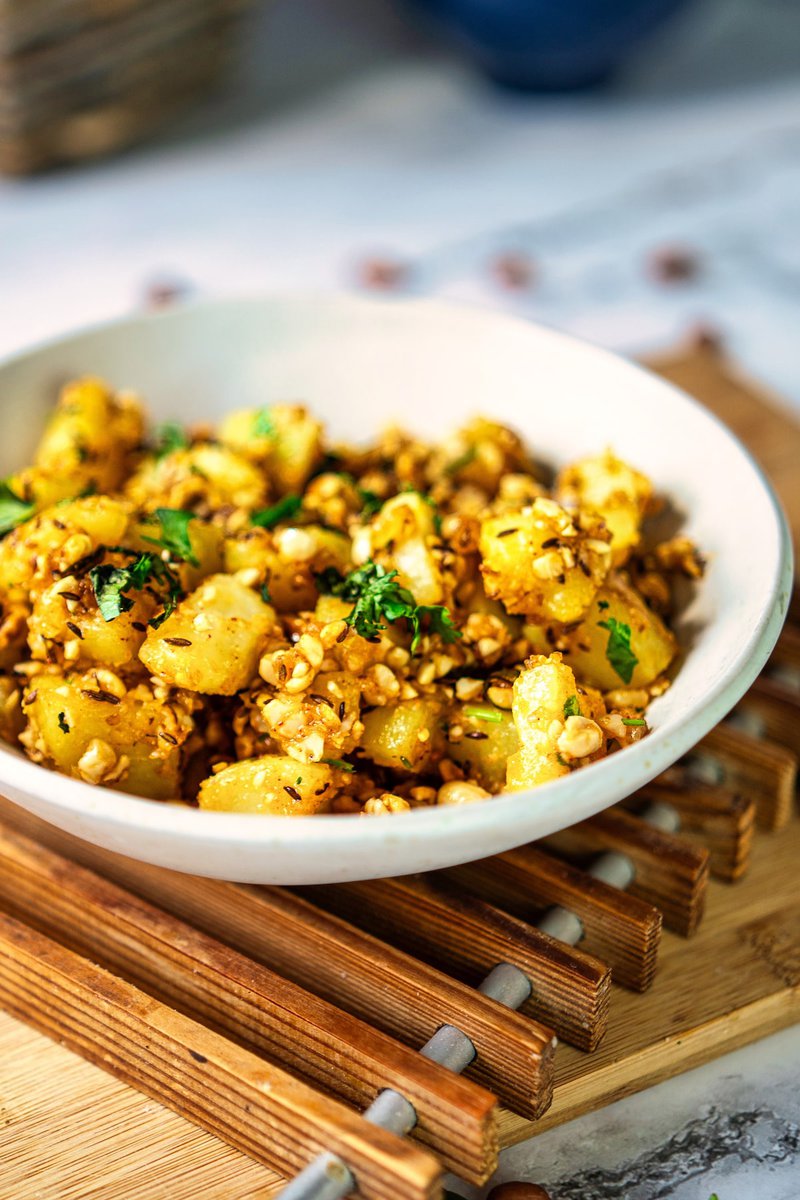 A closeup of bowl of vrat wale aloo, seasoned potatoes garnished with herbs and nuts.