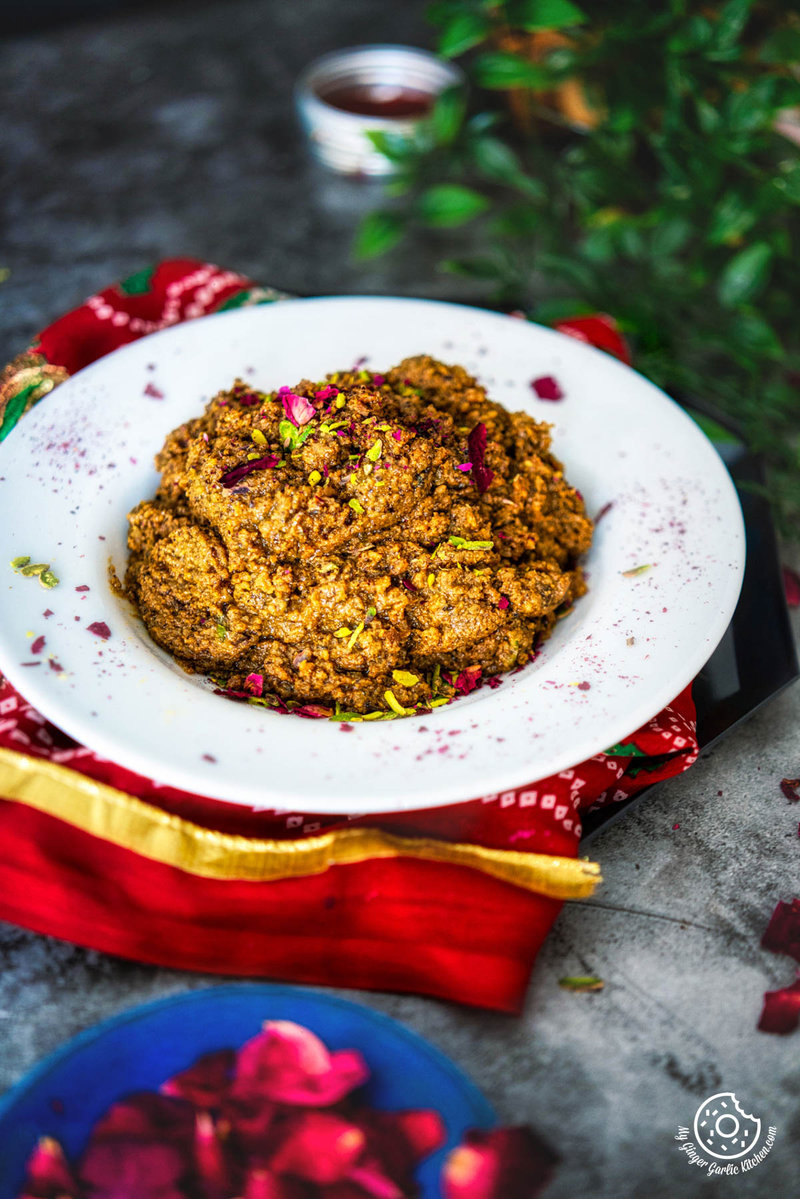 there is a plate of Walnut Halwa (Akhrot Halwa) on a red cloth and a plant in the background