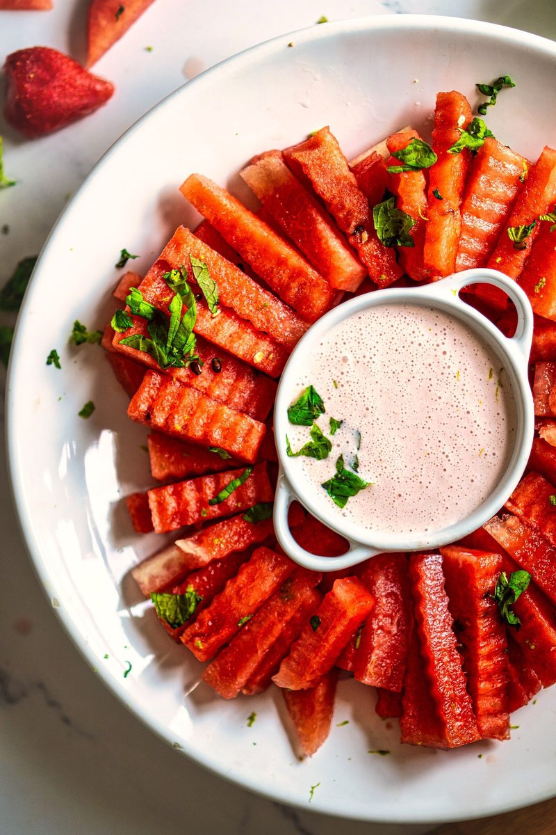 A top-down view of watermelon fries with strawberry yogurt dip in the center, sprinkled with mint and lime zest.