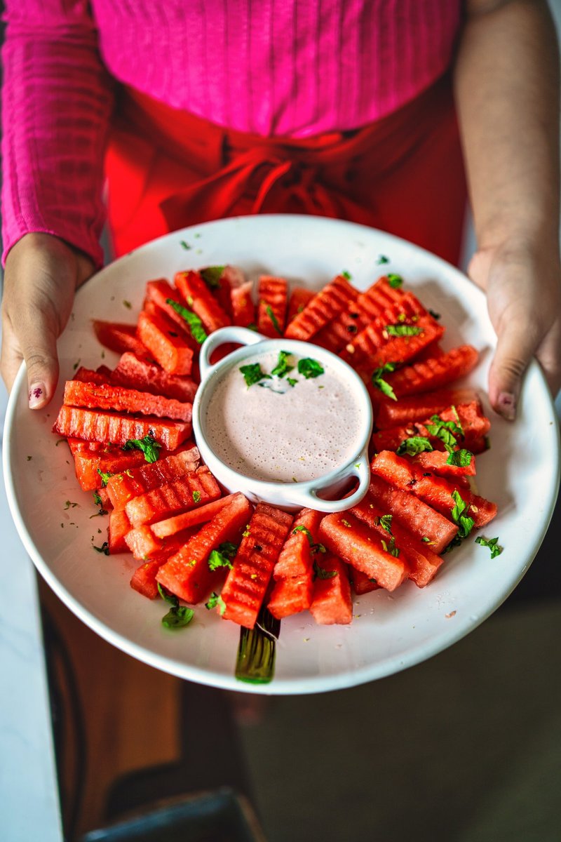 A person holding a plate of watermelon fries with strawberry yogurt dip, garnished with mint and lime zest.