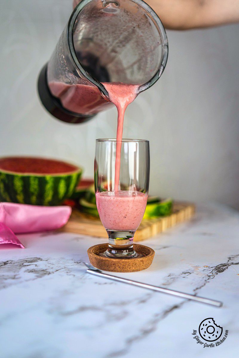 a hand pouring watermelon smoothie in a glass