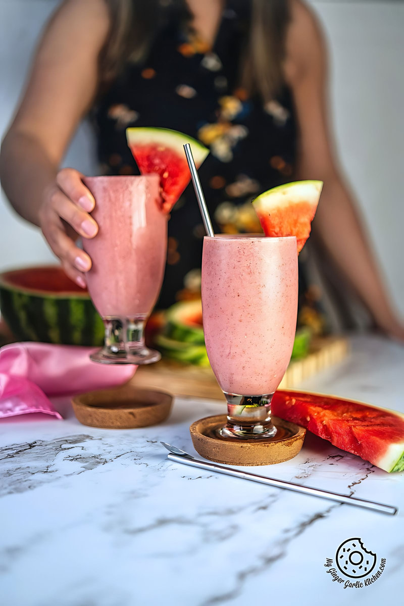 a a female holding a glass of watermelon smoothie and one more smoothie glass on the side