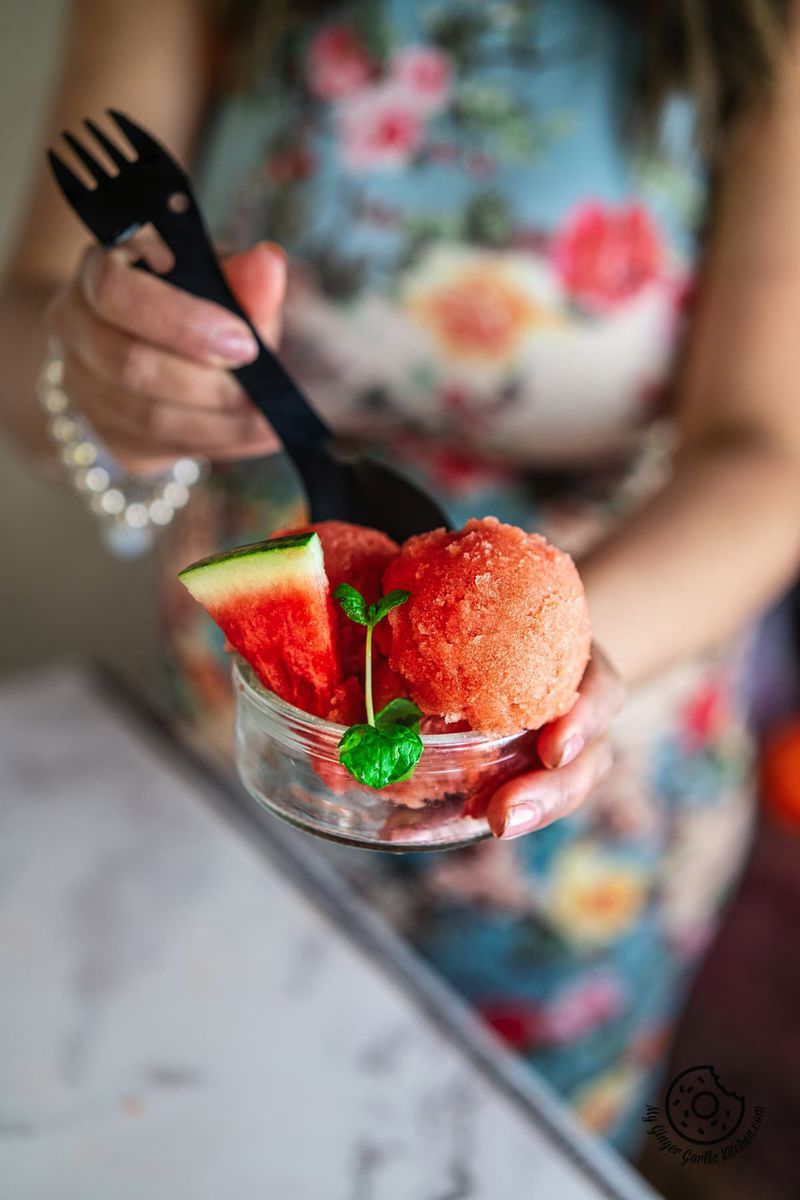 a female holding watermelon sorbet bowl with one hand and scooping it with a black spoon with other hand