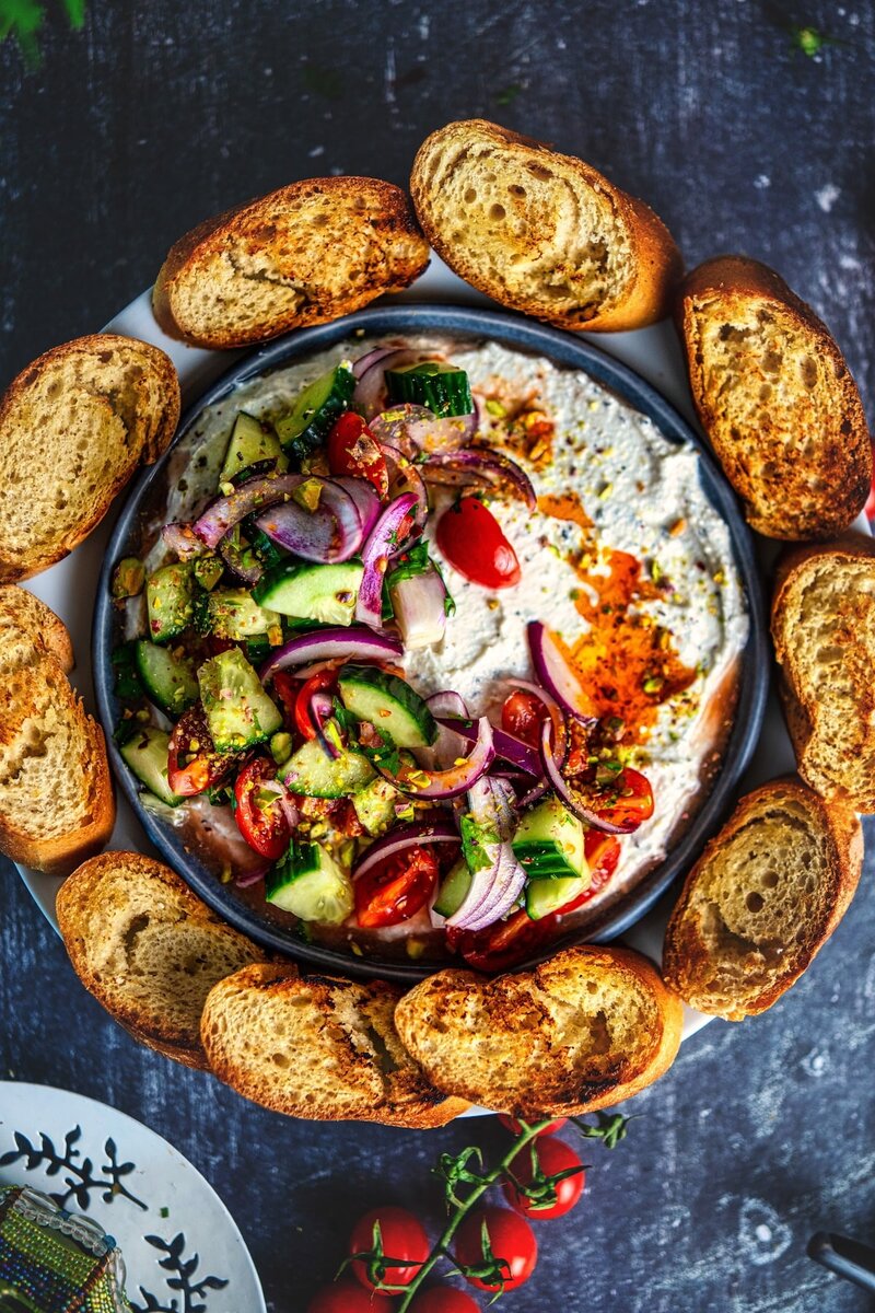 Overhead view of Mediterranean whipped cottage cheese dip with feta, tomato cucumber topping, and crispy toasted bread
