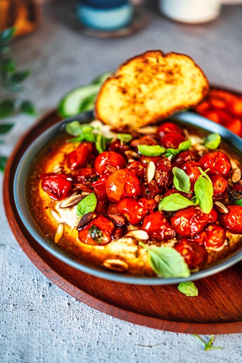 Homemade whipped feta appetizer with roasted tomatoes, toasted almonds, and fresh herbs served with grilled bread slices