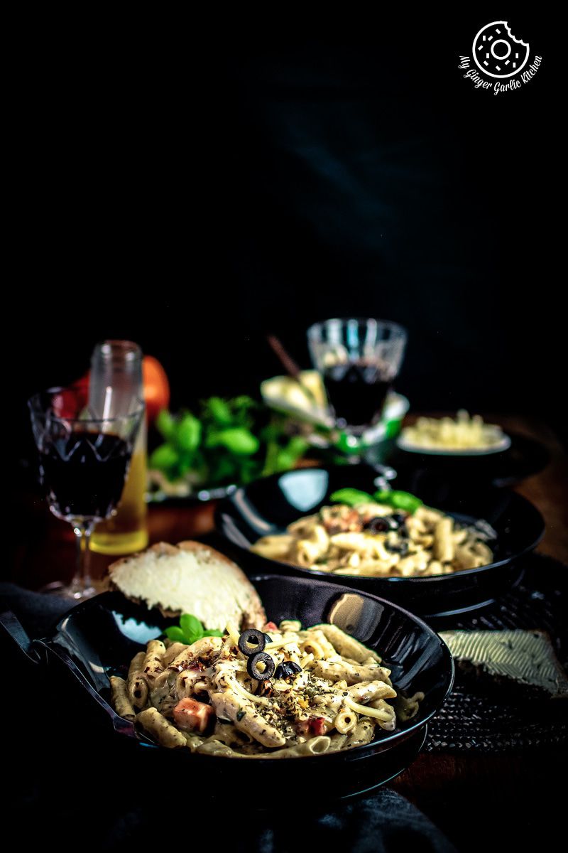 two plates of white sauce pasta with bread on the table, and two glasses on wine in the background