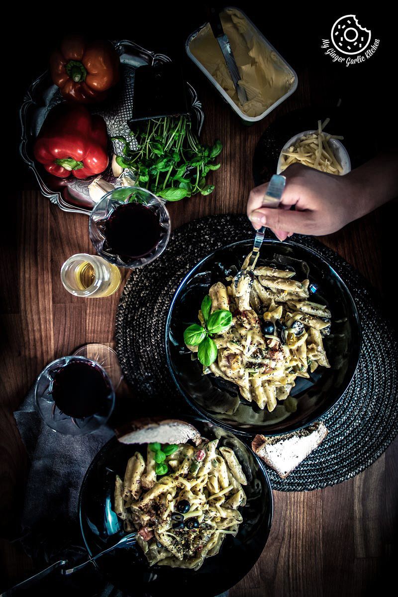 swhite sauce pasta in two bowls a two glasses of wine and some vegetables on side