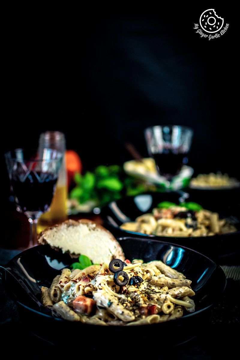 a plate of white sauce pasta with a piece of bread and two glasses of wine