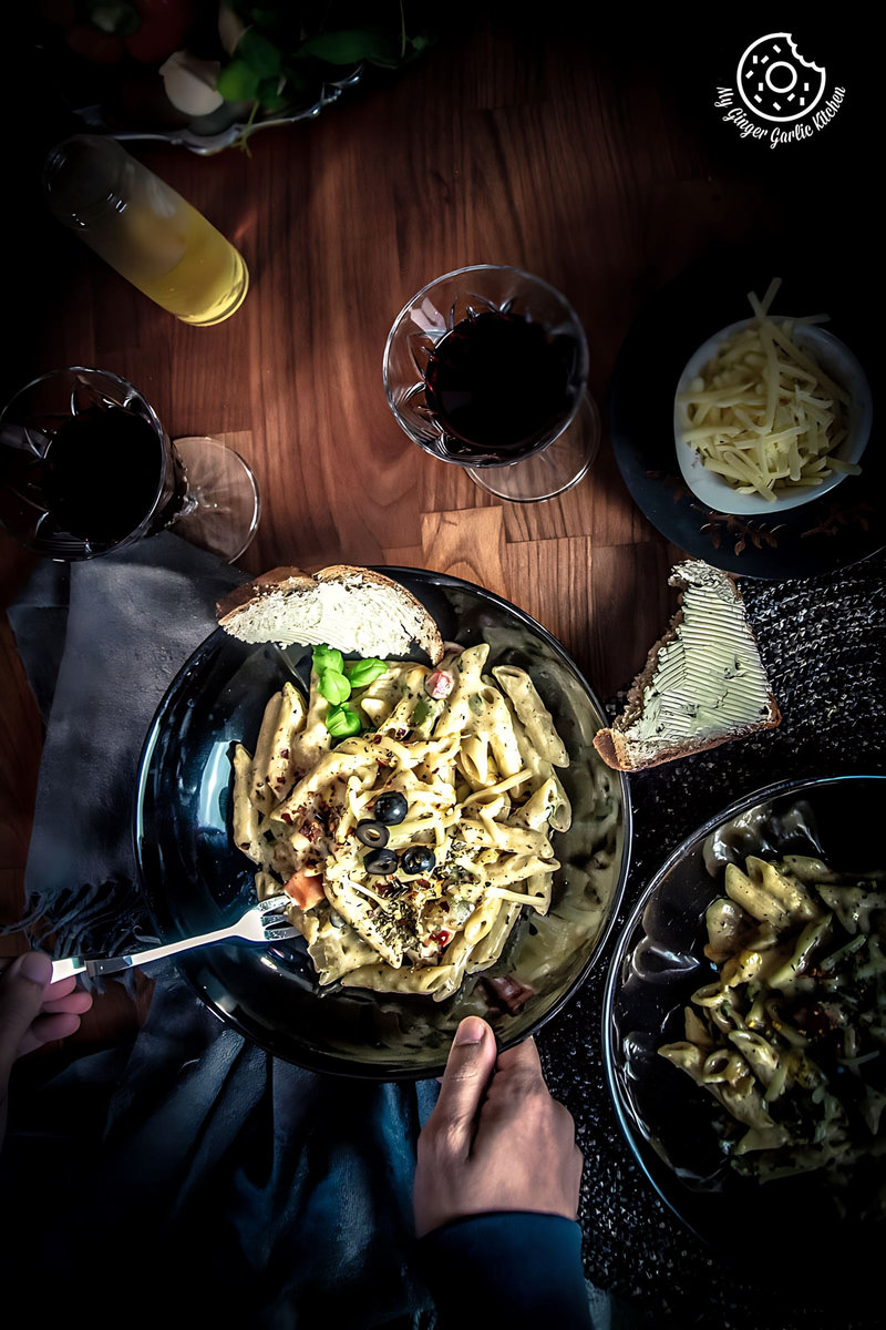 someone is eating white sauce pasta with a fork and a glass of wine