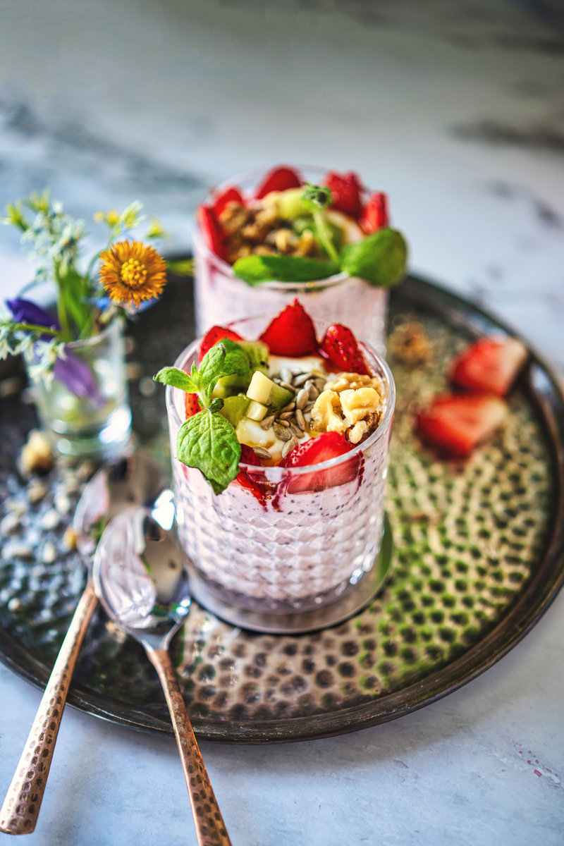 Two glasses of layered strawberry chia pudding topped with fresh berries and seeds.