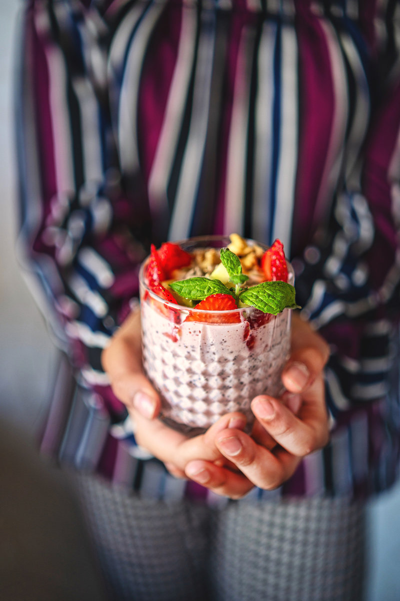 Person holding a glass of strawberry chia pudding topped with fresh berries and nuts.